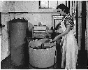 A woman operating a Rural Electrification Adminstration washing machine circa 1938